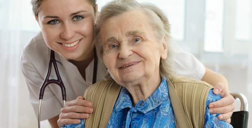 An older woman being hugged from behind by a healthcare professional