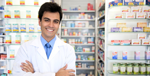 A male pharmacist stood with his arms crossed in front of medication shelves