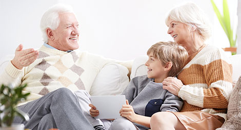 An older couple sat on a sofa with their grandson who is using a tablet